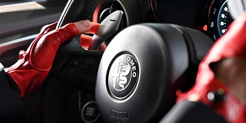 Red gloved hand gripping an Alfa Romeo steering wheels